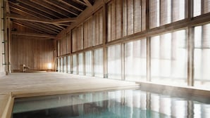 A traditional Japanese onsen with wooden beams, tatami flooring, and large sliding doors.