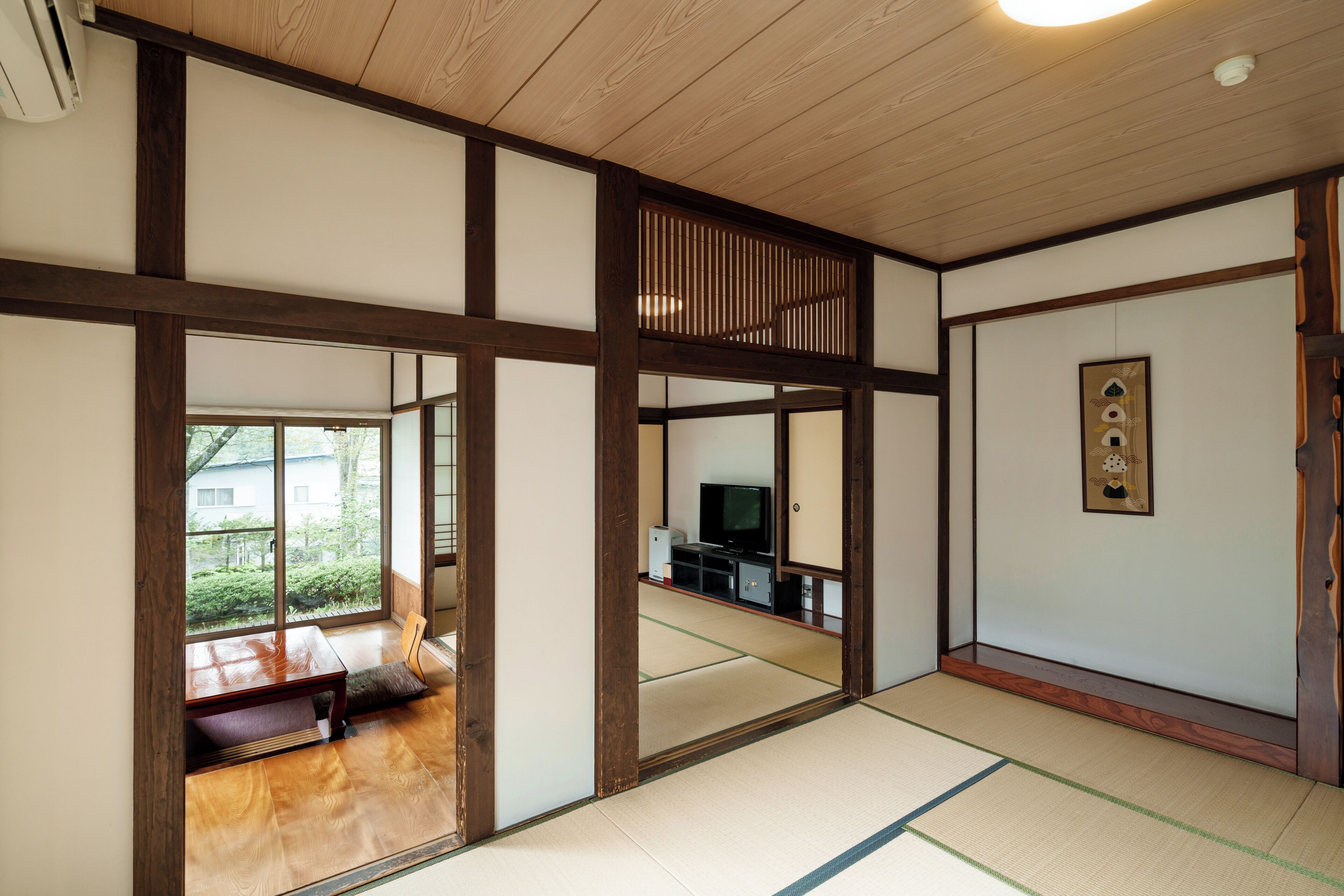A traditional Japanese room with tatami flooring, a television, and a sliding door leading to a balcony.
