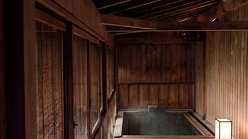 A wooden spa room with a hot tub, wooden walls, and a small table with a light.