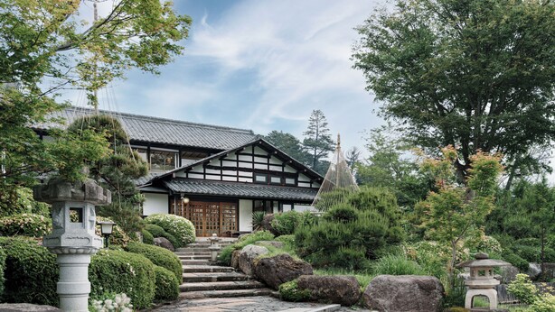 A traditional Japanese house with a tiled roof, wooden beams, and a stone lantern.