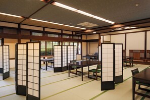 Um quarto japonês tradicional com tatames, painéis shoji e uma mesa baixa com cadeiras.