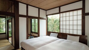 A traditional Japanese-style bedroom with tatami flooring, a low wooden bed, and a sliding shoji screen door.