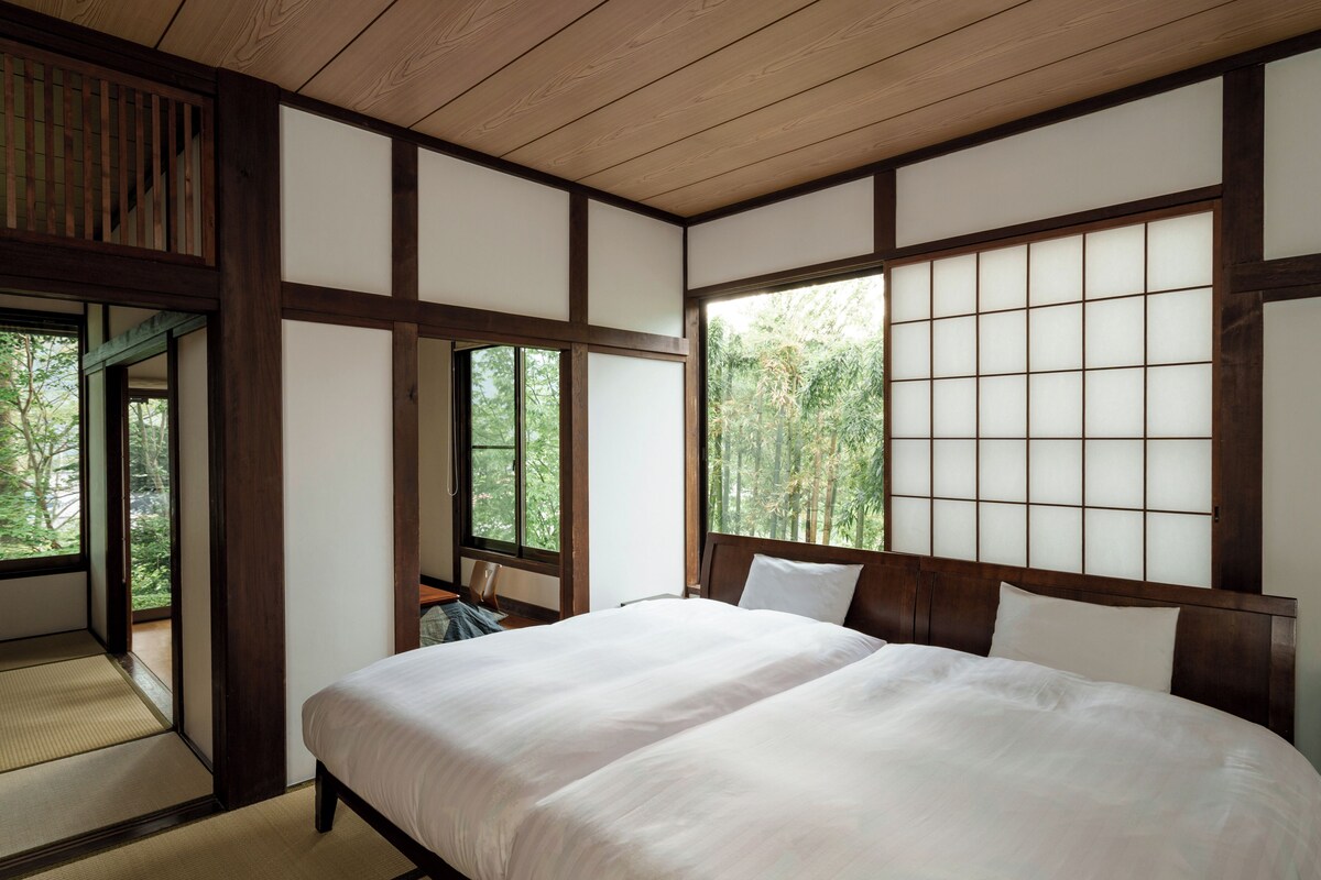 Quarto japonês tradicional com piso de tatame, cama de madeira baixa e porta de tela deslizante shoji.