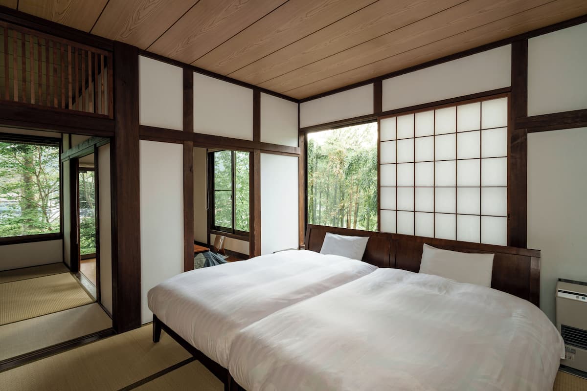 Ein traditionelles japanisches Schlafzimmer mit Tatami-Böden, einem großen Bett, Schiebetüren und Blick auf Bäume.