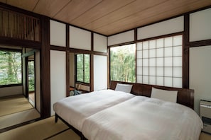 Ein traditionelles japanisches Schlafzimmer mit Tatami-Böden, einem großen Bett, Schiebetüren und Blick auf Bäume.