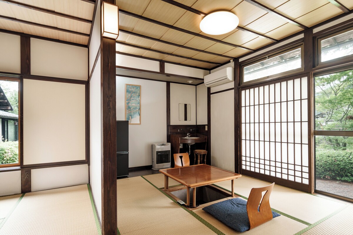 Quarto japonês tradicional com tatame, uma mesa de madeira baixa e uma porta deslizante com vista para o verde.