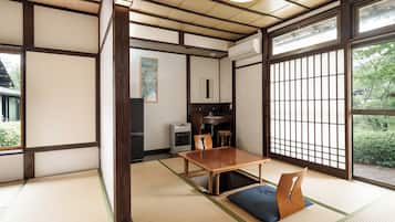 Une pièce de style japonais traditionnel, avec un sol recouvert de tatamis, une petite table en bois et une porte coulissante donnant sur un paysage verdoyant.