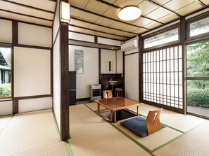 Quarto japonês tradicional com tatame, uma mesa de madeira baixa e uma porta deslizante com vista para o verde.