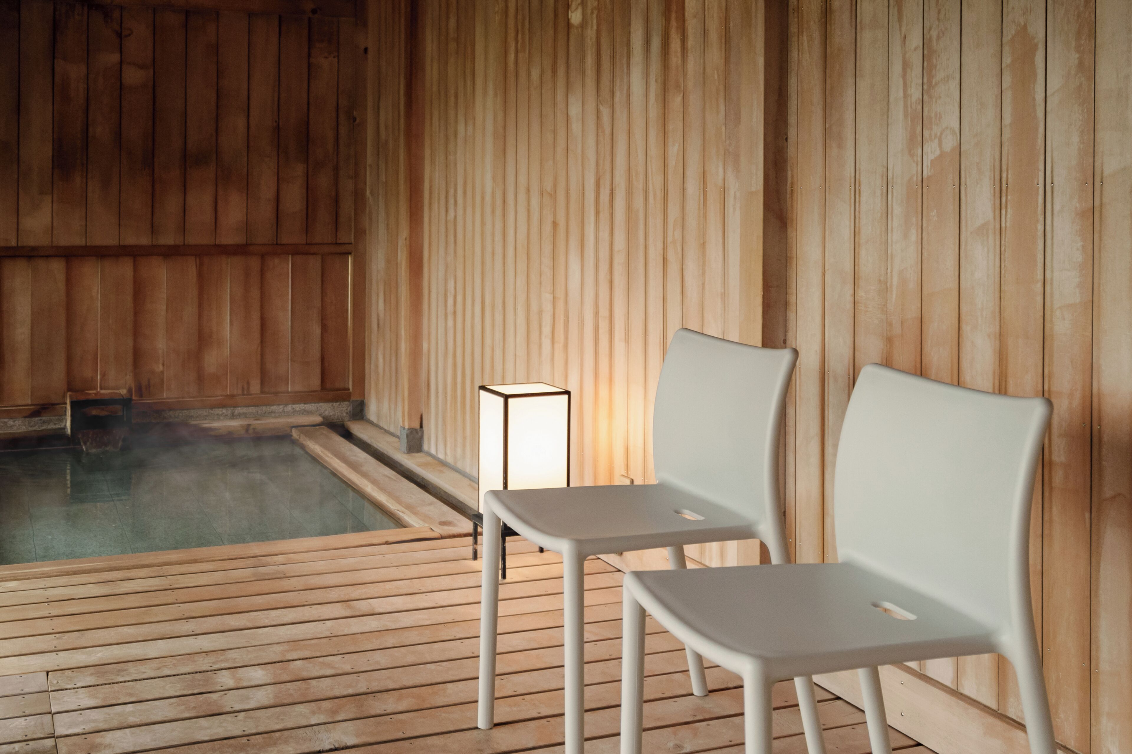 Un sauna en bois avec deux chaises blanches et une petite table, un plancher en bois et un jacuzzi visible.
