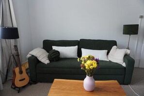 A room with a dark green sofa, a wooden coffee table, a guitar, and a vase with flowers. - Cosy 1BDR | Central Brighton | Near Station (Brighton and Hove)