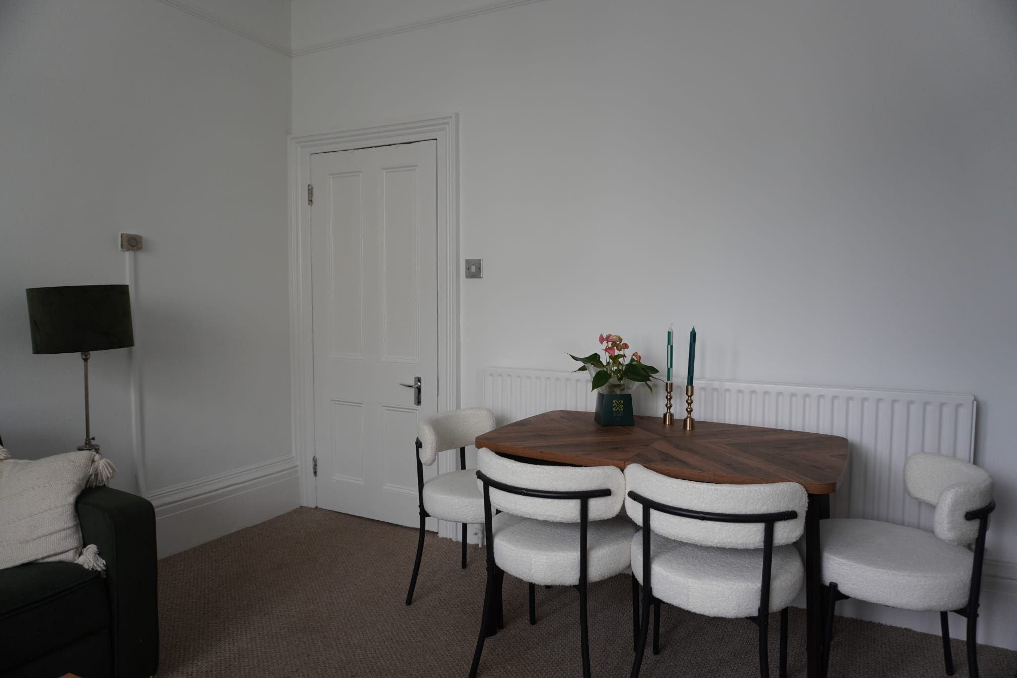 A room with a dining table, four chairs, a black floor lamp, a white door, and a radiator.