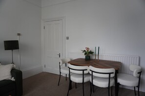 Une pièce comprenant une table à manger, quatre chaises, un lampadaire noir, une porte blanche et un radiateur.