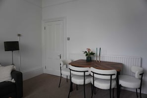 Ein Zimmer mit einem Holzesstisch, vier weißen Stühlen, einer schwarzen Stehlampe und einer weißen Tür.