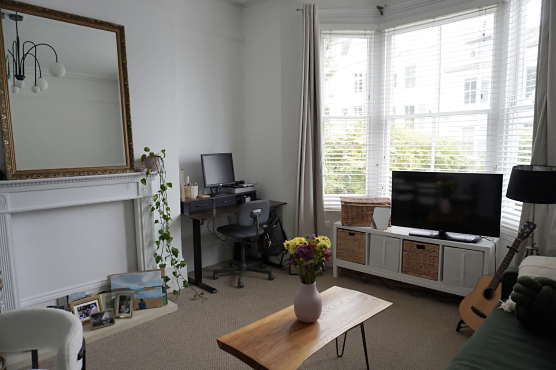 A living room with a fireplace, a desk with a computer, a television, and a guitar.