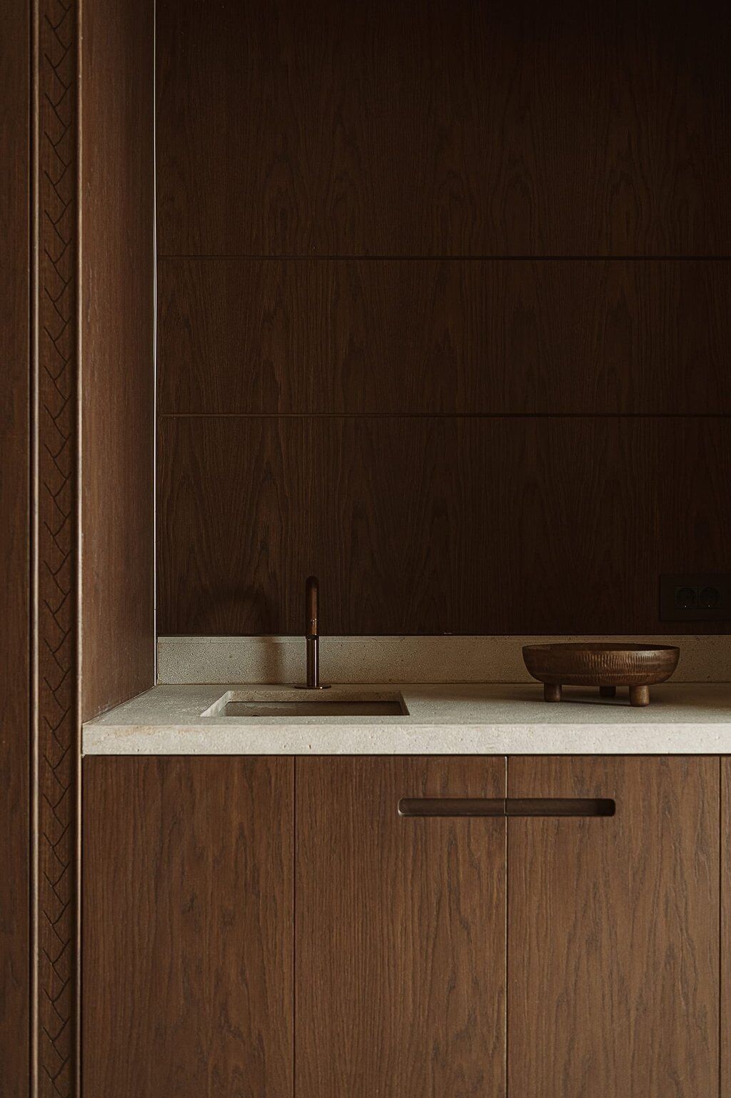 Een keuken met houten kastjes, een aanrecht, een spoelbak en een kleine houten kom.
