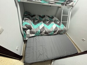 A compact room with a bunk bed, a small table, and a power outlet on the wall.