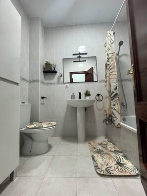 A bathroom with a toilet, sink, shower, and a mirror.