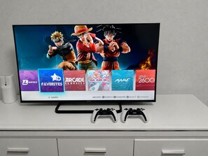 A television displaying video game titles and two game controllers on a white surface.