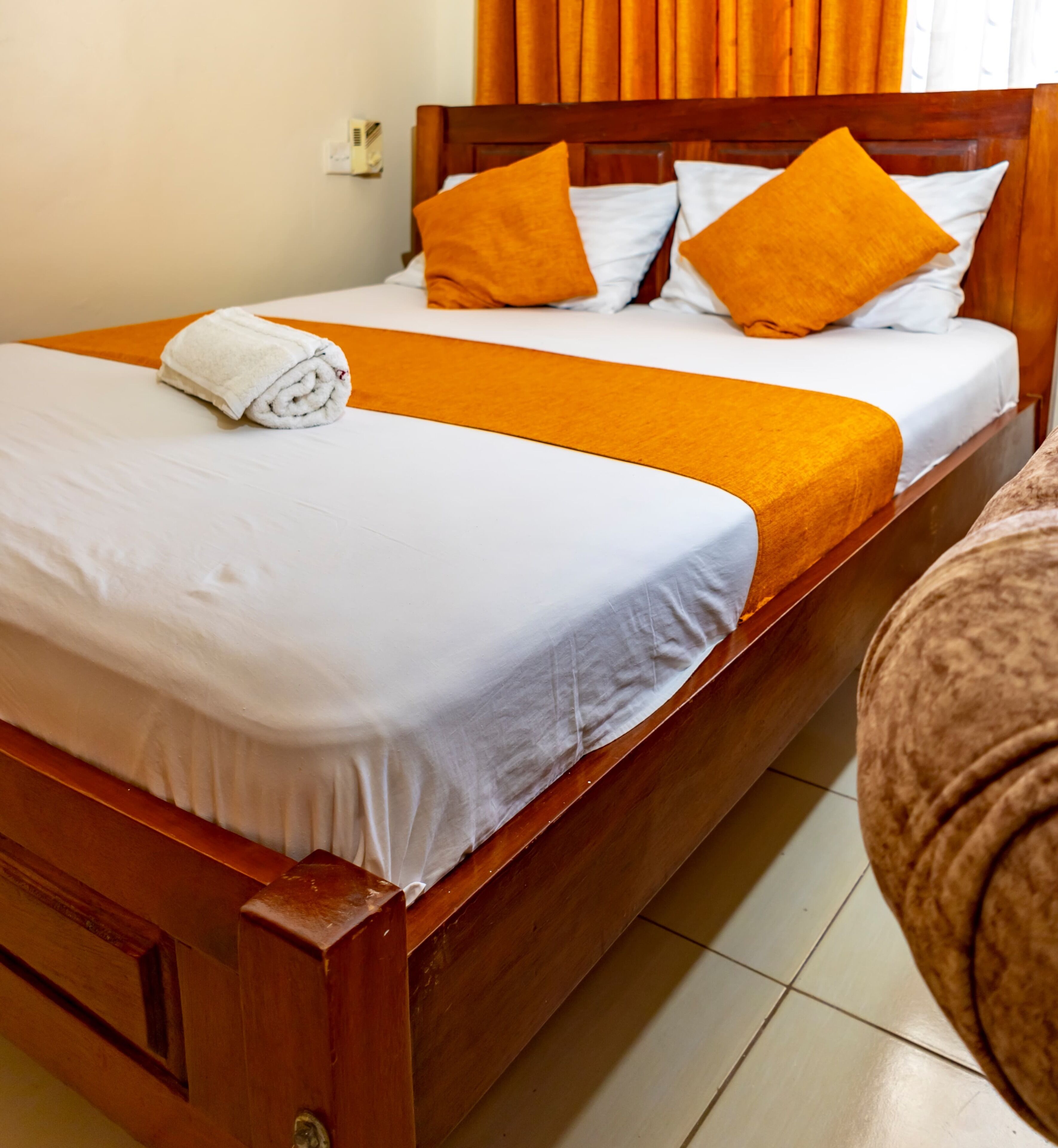 Un lit double avec du linge de lit blanc, un plaid orange et deux oreillers orange.