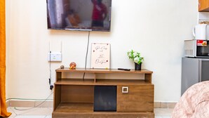 A modern living room with a flat-screen TV mounted on the wall, a wooden entertainment unit with a small shelf, a power outlet, and a framed motivational quote. - Curated modern studio in mombasa Nyali, 5 mins drive to nyali beach (Mombasa)