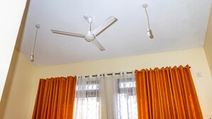 A ceiling fan, a window with orange curtains, and a wall socket. - Curated modern studio in mombasa Nyali, 5 mins drive to nyali beach (Mombasa)