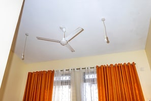 Ein Deckenventilator, ein Fenster mit orangefarbenen Vorhängen und eine Steckdose.