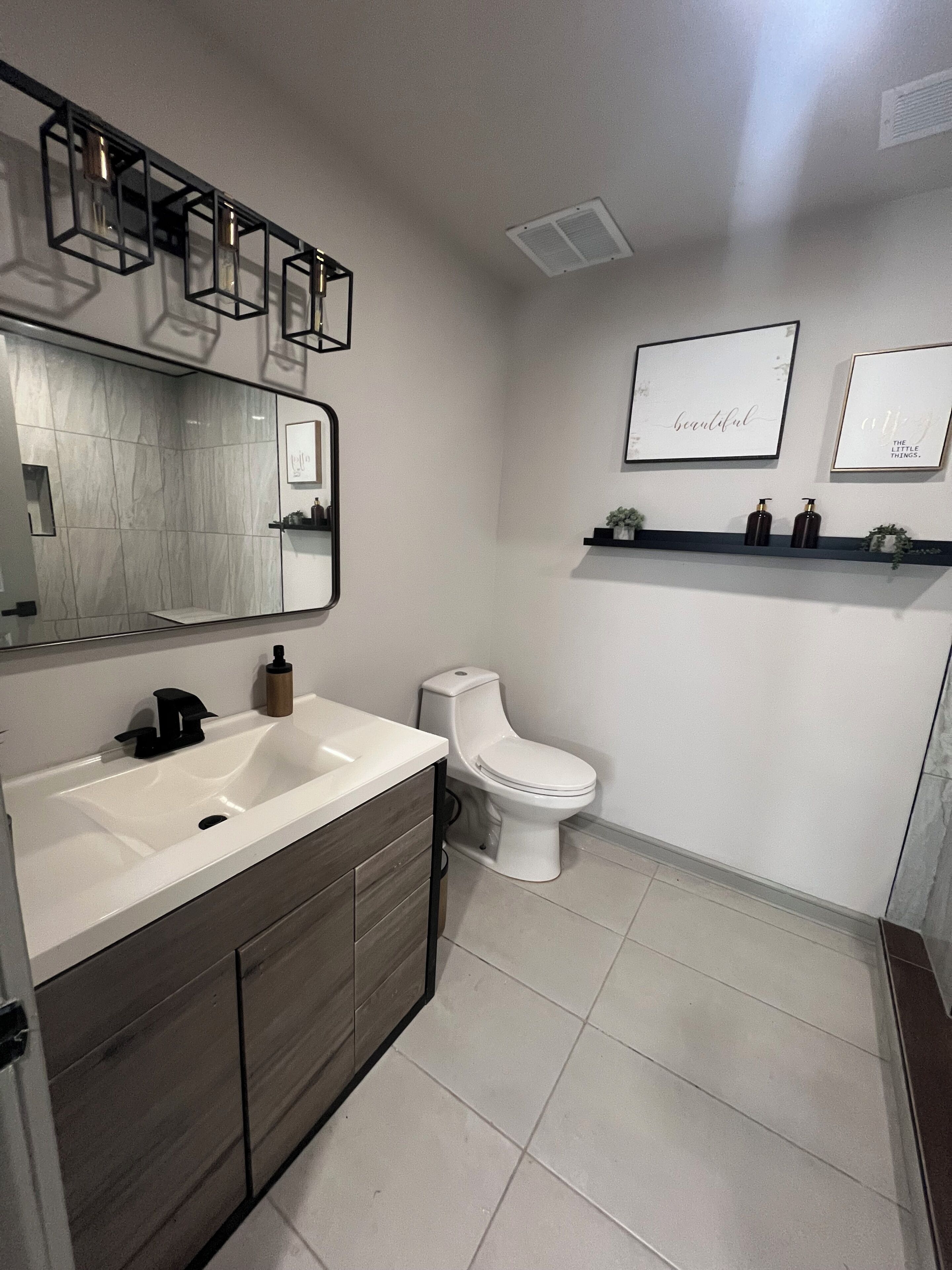 A modern bathroom with a large mirror, a white sink, a toilet, and two framed motivational quotes on the wall.