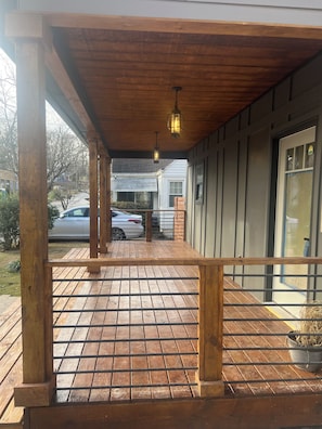 Eine überdachte Holzterrasse mit Geländer, ein geparktes Auto im Hintergrund und ein Haus mit einer Garagentür.