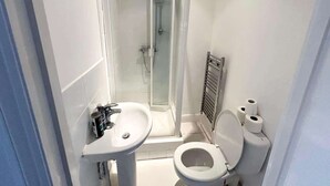 Een kleine, moderne badkamer met een douchecabine van glas, een wastafel op een voetstuk en een toilet.