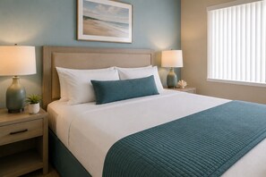 Un letto rifatto con cura, una coperta color petrolio, due lampade ai comodini, un comodino con una pianta e un quadro appeso al muro.