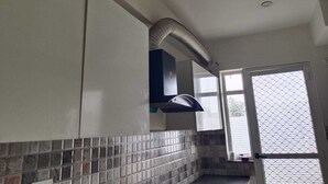 Eine Küche mit gefliestem Fliesenspiegel, einer schwarzen Dunstabzugshaube und einem Fenster mit Insektenschutzgitter.
