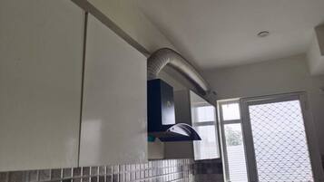 Eine Küche mit gefliestem Fliesenspiegel, einer schwarzen Dunstabzugshaube und einem Fenster mit Insektenschutzgitter.