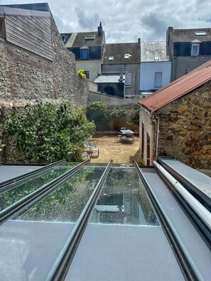 Un estrecho callejón con techo de vidrio, paredes de piedra y un pequeño patio con una mesa y sillas.
