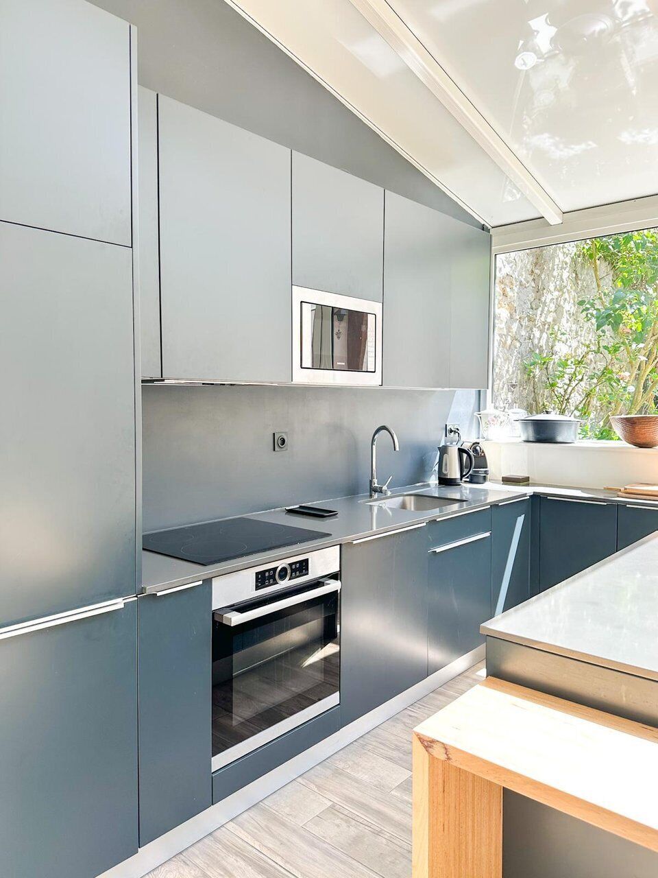 Een moderne keuken met grijze kastjes, een ingebouwde oven, een magnetron en een spoelbak.