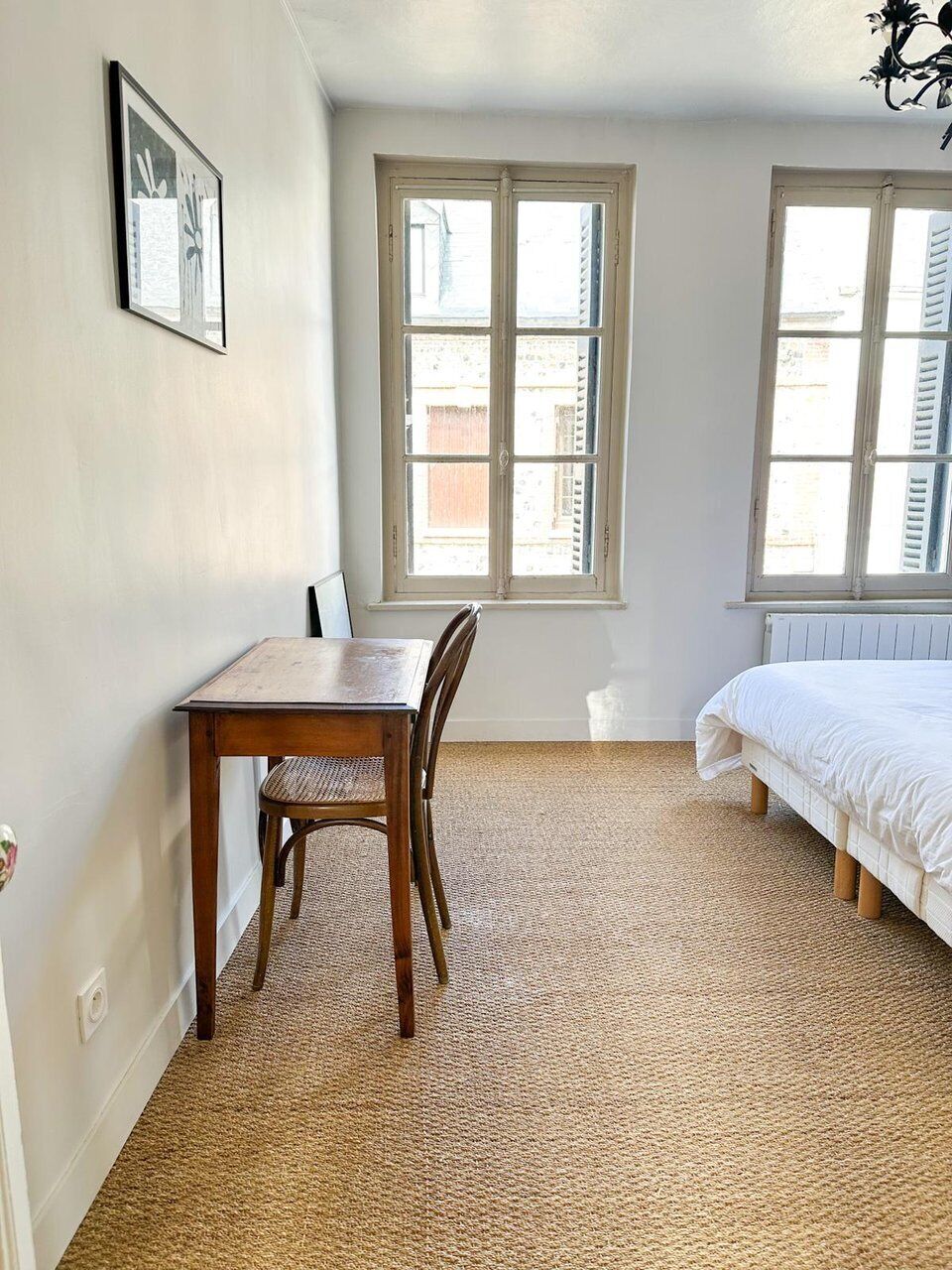 A room with a bed, a table, two windows, and a radiator.