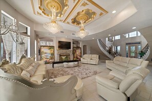 A luxurious living room with a fireplace, elegant furniture, and a grand chandelier.
