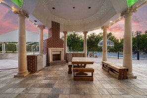 An outdoor patio with a brick fireplace, wooden benches, and string lights.