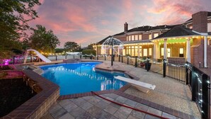 A swimming pool with a slide, surrounded by a brick patio, and a building with a brick facade and lights.