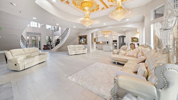 A spacious living area with a grand staircase, elegant furniture, and a chandelier.