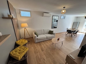 En stue med sofa, sofabord, lampe, tv og et spiseområde med stole.