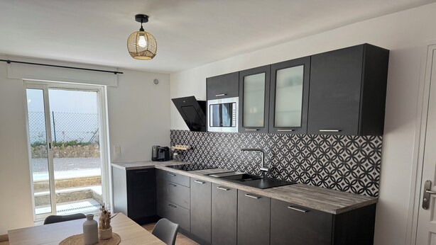 A modern kitchen with dark cabinets, a patterned backsplash, and a dining area with a wooden table and chairs. - Cocoon renovated Grasse (Grasse)