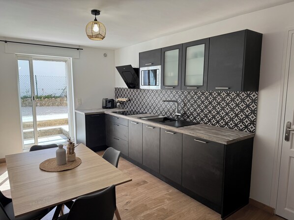A modern kitchen with dark cabinets, a patterned backsplash, and a dining area with a wooden table and chairs. - Cocoon renovated Grasse (Grasse)