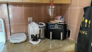 Eine Küche mit Kaffeemaschine, Reiskocher, einem schwarzen Gerät mit Bedienfeld und einem Reisbeutel auf der Arbeitsfläche.