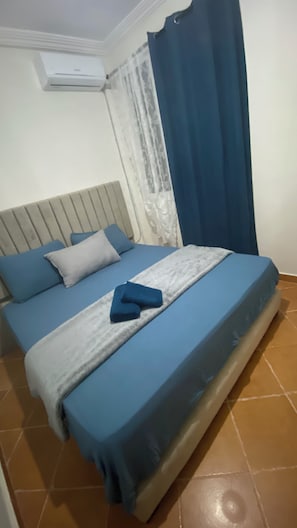 Ein Schlafzimmer mit Bett, Kissen, Decke, Vorhang und Klimaanlage.