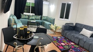 Ein Wohnzimmer mit einer Sofagarnitur, einem Esstisch mit Stühlen, einem Couchtisch und einem dekorativen Teppich.