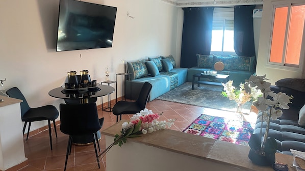 Ein Wohnzimmer mit einer Couch, einem Couchtisch, einem an der Wand befestigten Fernseher und einem Essbereich mit Stühlen und Tisch.