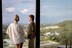 Two people standing by a window overlooking a cityscape and greenery. - Villa Kyma Uluwatu (Uluwatu)