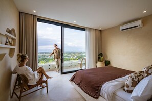Un dormitorio con una cama grande, un sofá, un balcón con vistas y un equipo de aire acondicionado.