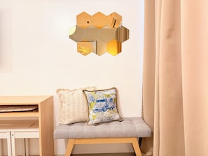 A bench with two pillows, a wall-mounted hexagonal mirror, and a wooden desk. - Cozy 1-bedroom condo in peaceful Pasay City with AC (Pasay City)