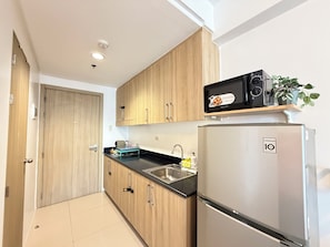 A modern kitchen with wooden cabinets, a stainless steel refrigerator, a microwave, and a sink. - Cozy 1-bedroom condo in peaceful Pasay City with AC (Pasay City)